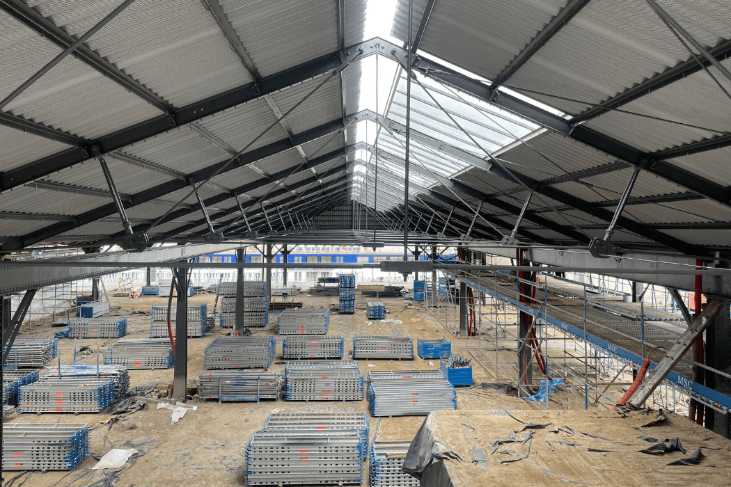 zicht vanbinnen uit, onder het metalen dak, met aanwezig bouwmateriaal
